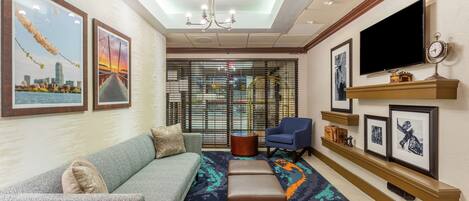 A hotel lobby with a sofa, ottoman, and armchair, a television, and framed pictures on the walls.