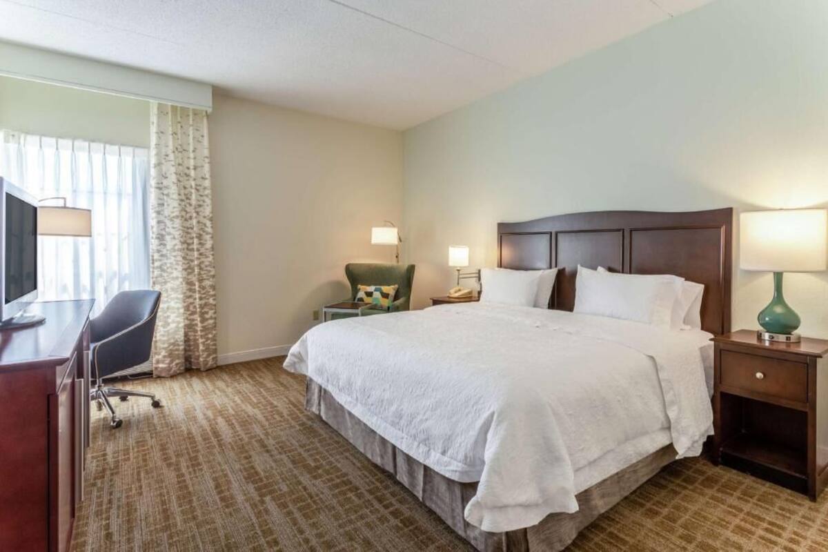 A hotel room with a bed, desk, chair, and lamps.