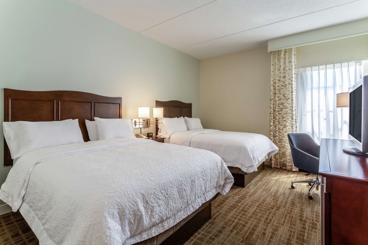 A hotel room with two beds, a desk, a chair, and a TV.