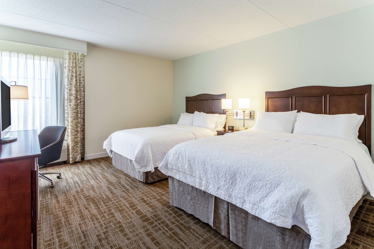 A hotel room with two beds, a desk, and a chair.