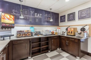 A bakery counter with a chalkboard displaying 'EAT' and 'BAKE', a coffee machine, and various baked goods.