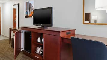 Habitación de hotel con un escritorio de madera, televisor, minibar y espejo.