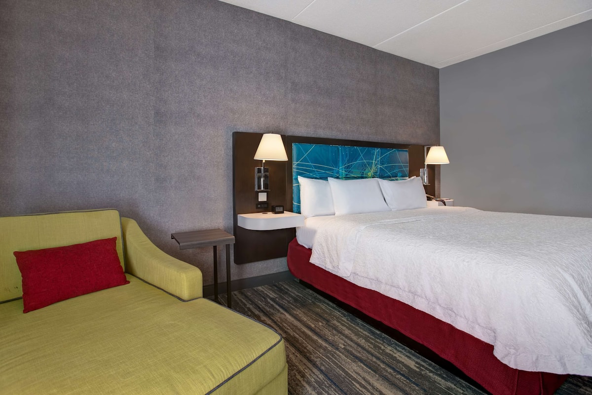 Quarto de hotel com cama, sofá, mesa de cabeceira e abajur.
