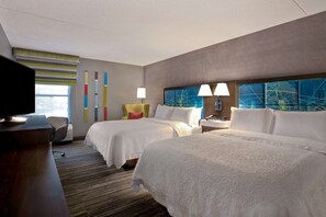 Habitación de hotel con dos camas, un escritorio, un televisor y una ventana con persianas.