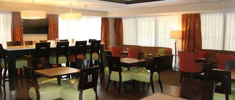 Comedor de hotel con varias mesas y sillas, un sofá y una pantalla de televisión.