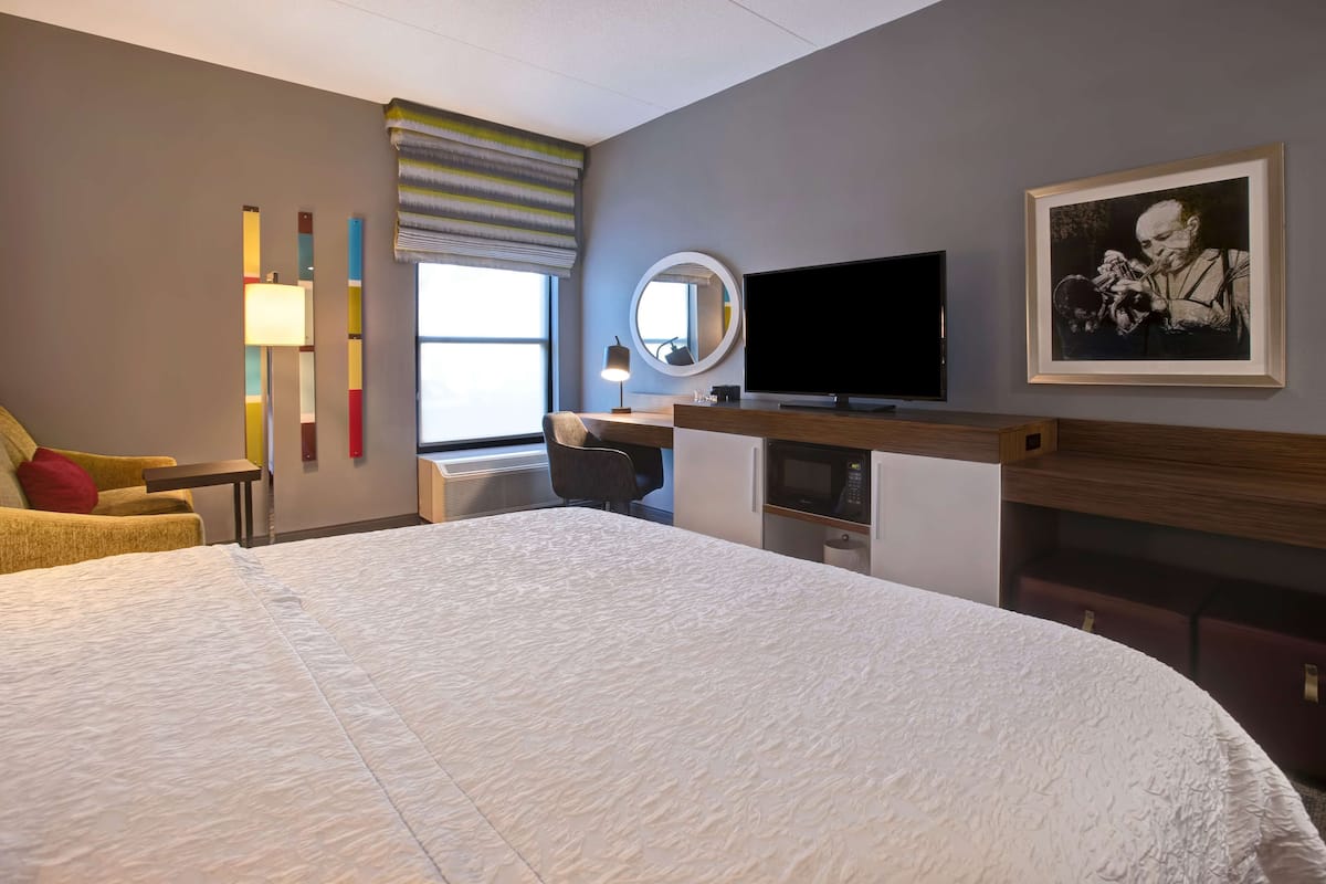 Quarto de hotel com uma cama grande, uma mesa com televisão de tela plana, micro-ondas e uma obra de arte emoldurada na parede.