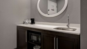 A modern bathroom with a white sink, a round mirror, a coffee maker, and a microwave. - Hampton Inn Olive Branch (Olive Branch)