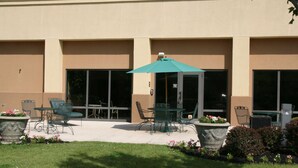 An outdoor patio area with tables and chairs, a covered seating area, and planters with flowers. - Hampton Inn Olive Branch (Olive Branch)