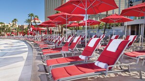 Un área junto a la playa con hileras de sillas y sombrillas rojas y blancas.