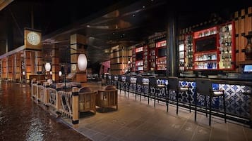 Una zona de bar con mobiliario de madera, suelo de baldosas y una barra con estantes llenos de botellas.