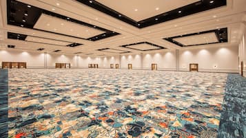 Un salón de conferencias amplio con alfombra estampada, iluminación empotrada y un techo alto.