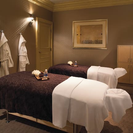 A spa room with two massage tables, towels, a water bottle, and a framed artwork on the wall.