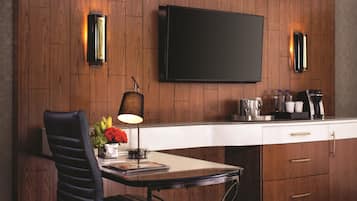 A modern kitchen with a wooden wall, a flat-screen TV, a coffee machine, and a dining area with a table and chair.
