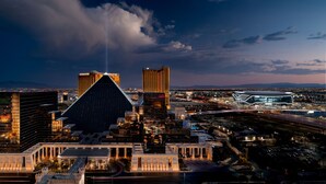 Un paisaje urbano al anochecer con edificios modernos destacados, incluyendo una estructura en forma de pirámide y un gran edificio iluminado con un letrero de 'W'.
