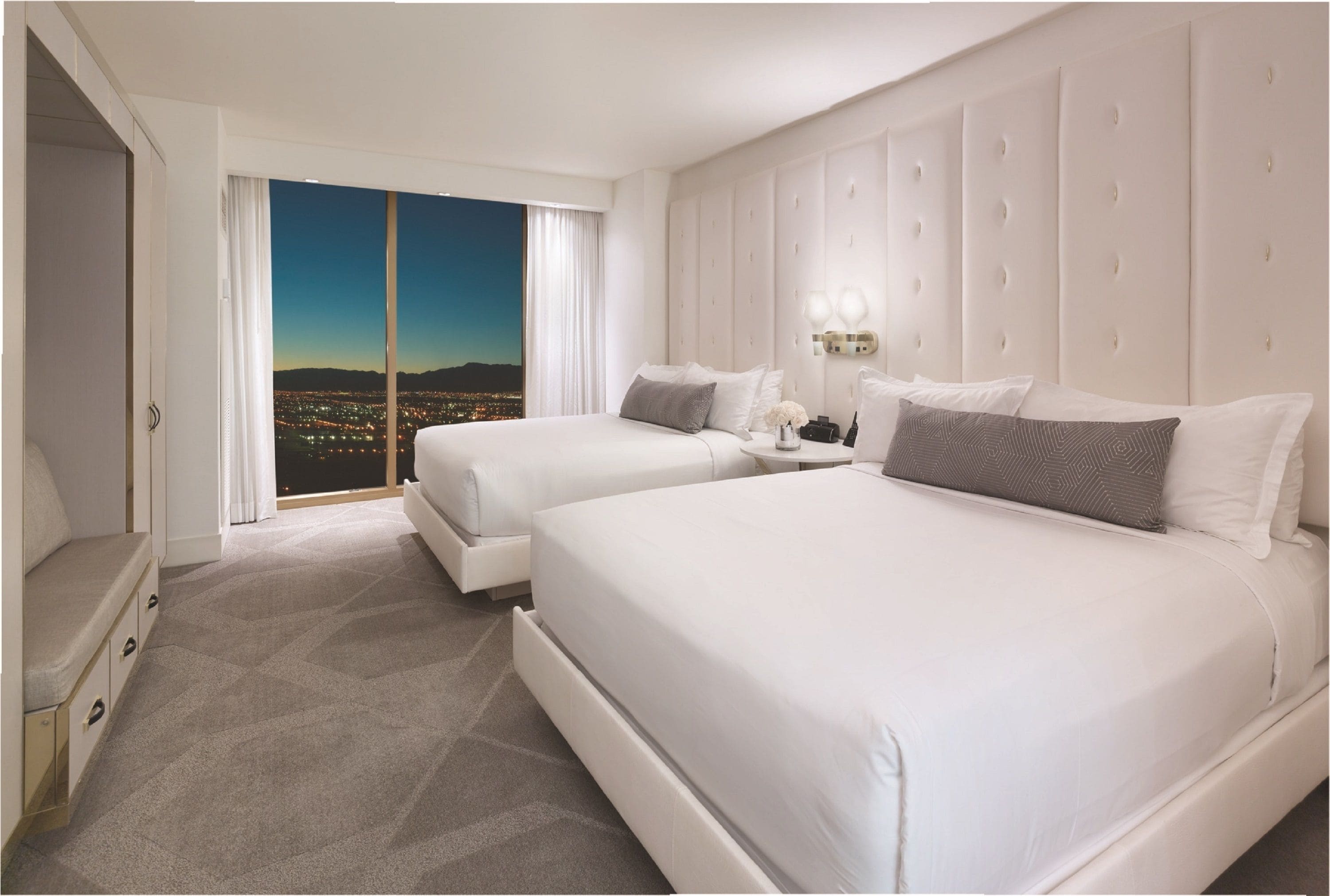 A hotel room with two beds, a large window with a city view, and a white color scheme.