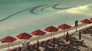 Una zona en la playa con hileras de sombrillas rojas y sillas reclinables orientadas al océano.