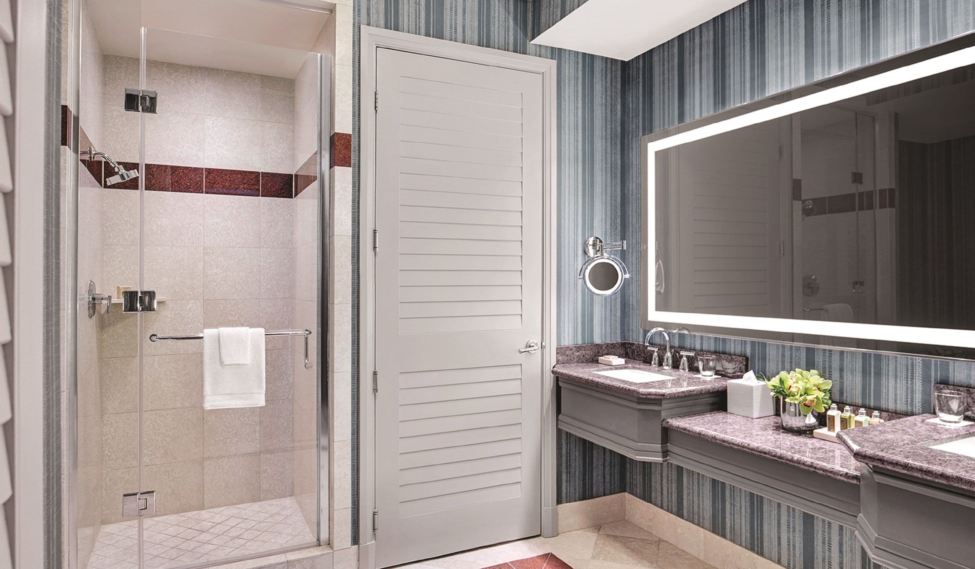 A modern bathroom with a walk-in shower, a large mirror, and a vanity with a marble countertop.