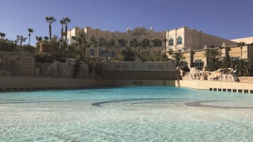 Un área de piscina con agua cristalina, palmeras y un edificio con un letrero que dice 'Mandalay Bay Convention Center'.