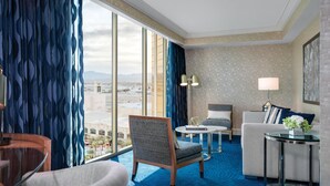 A hotel room with a large window, a sofa, a chair, a small table, and a lamp.