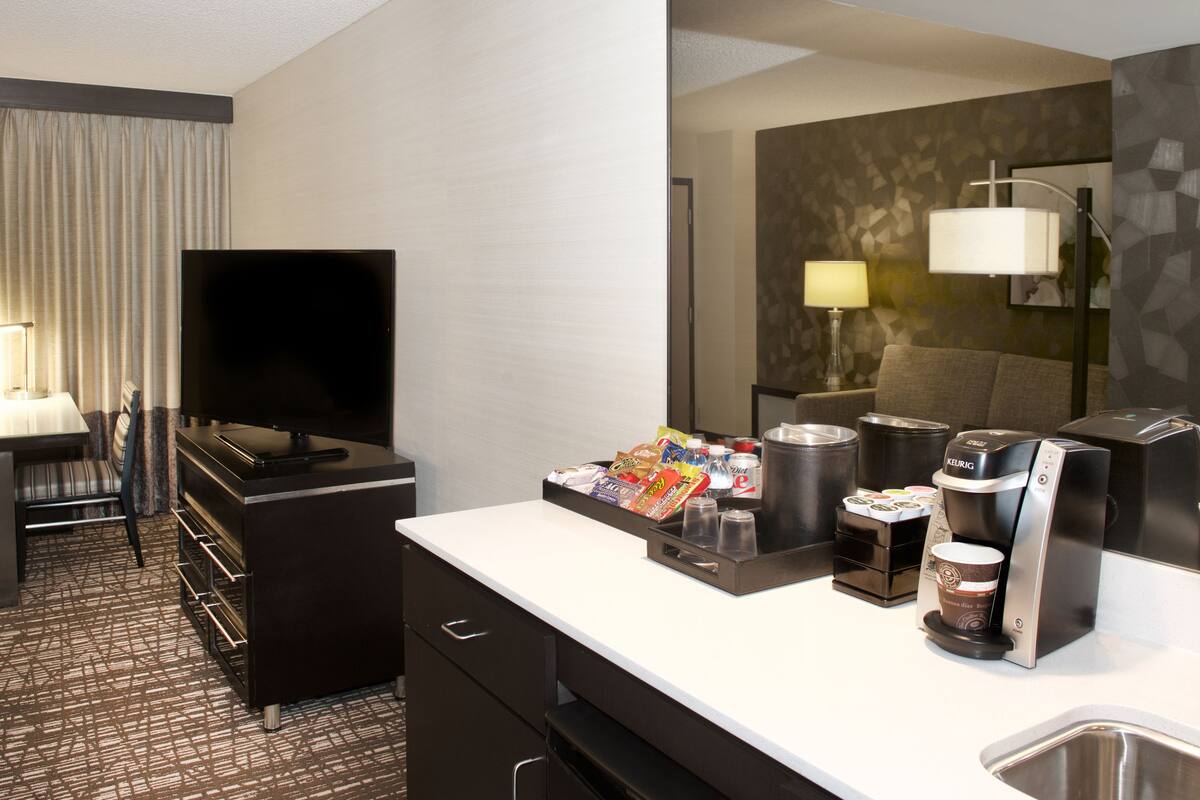 Een hotelkamer met een flatscreen televisie, een bureau met lamp, een minibar en een koffiezetapparaat.
