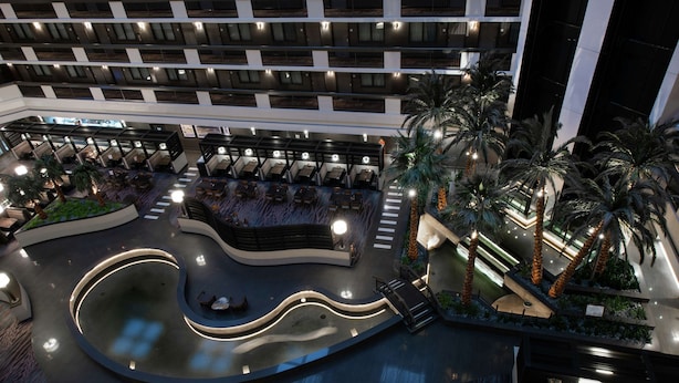 A hotel atrium with multiple floors of balconies, a central pool area, and outdoor seating with palm trees. - Embassy Suites by Hilton Las Vegas (Las Vegas)