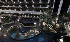 Um átrio de hotel com vários andares de varandas, área de piscina central e mobiliário de jardim com palmeiras.
