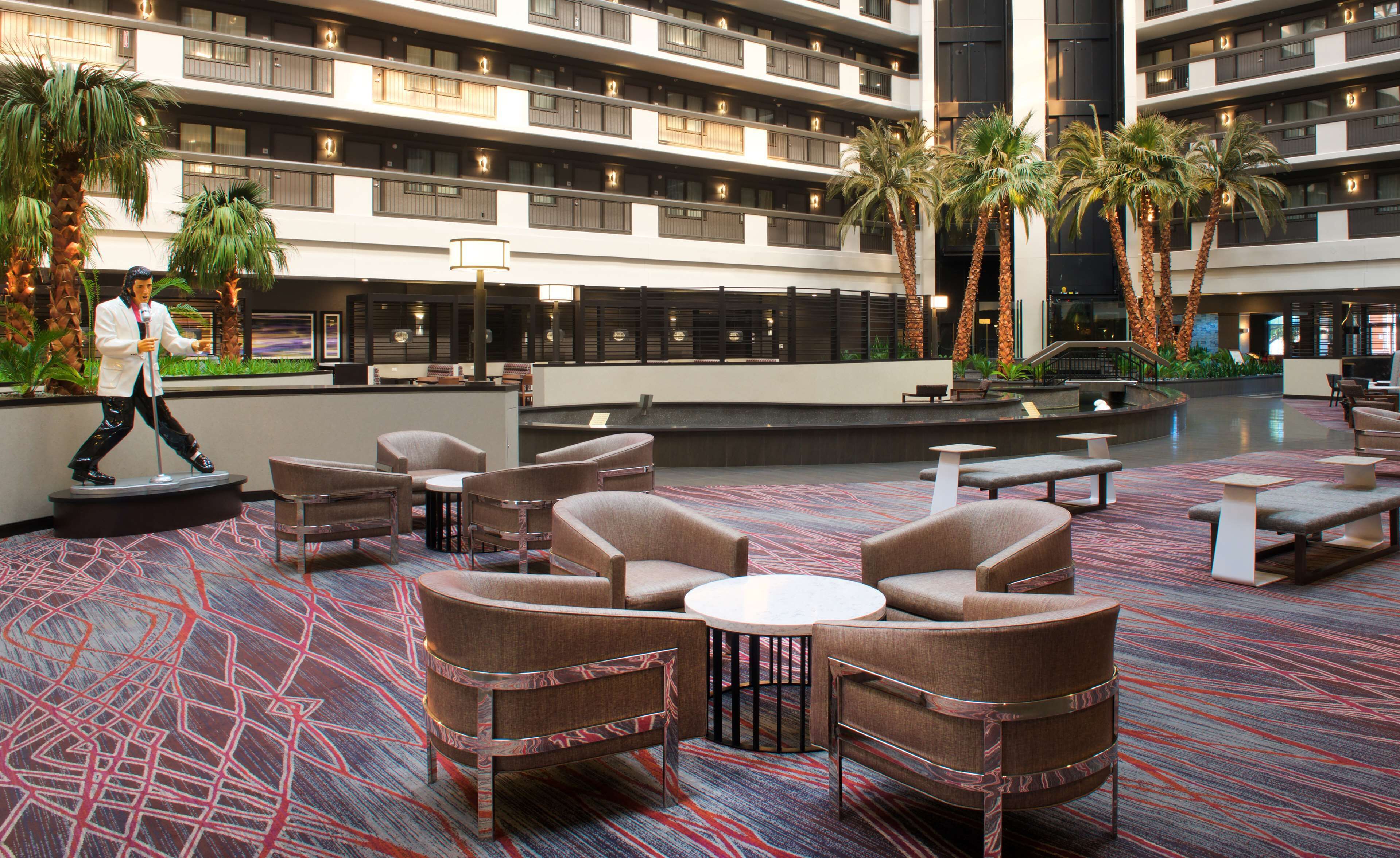 Un vestíbulo de hotel con varios pisos, palmeras y zonas de estar.