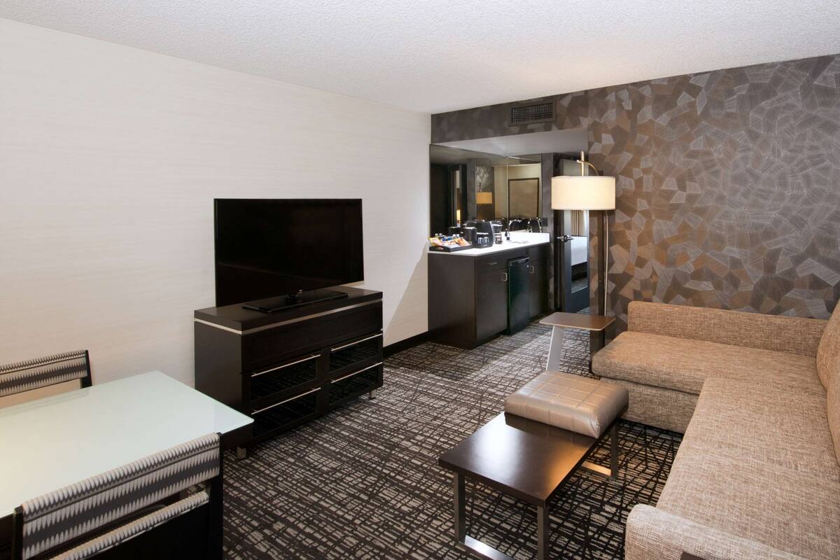 Hotelkamer met flatscreen televisie, een bank, een klein tafeltje, een koffiehoekje en een kamerbreed tapijt met dessin.
