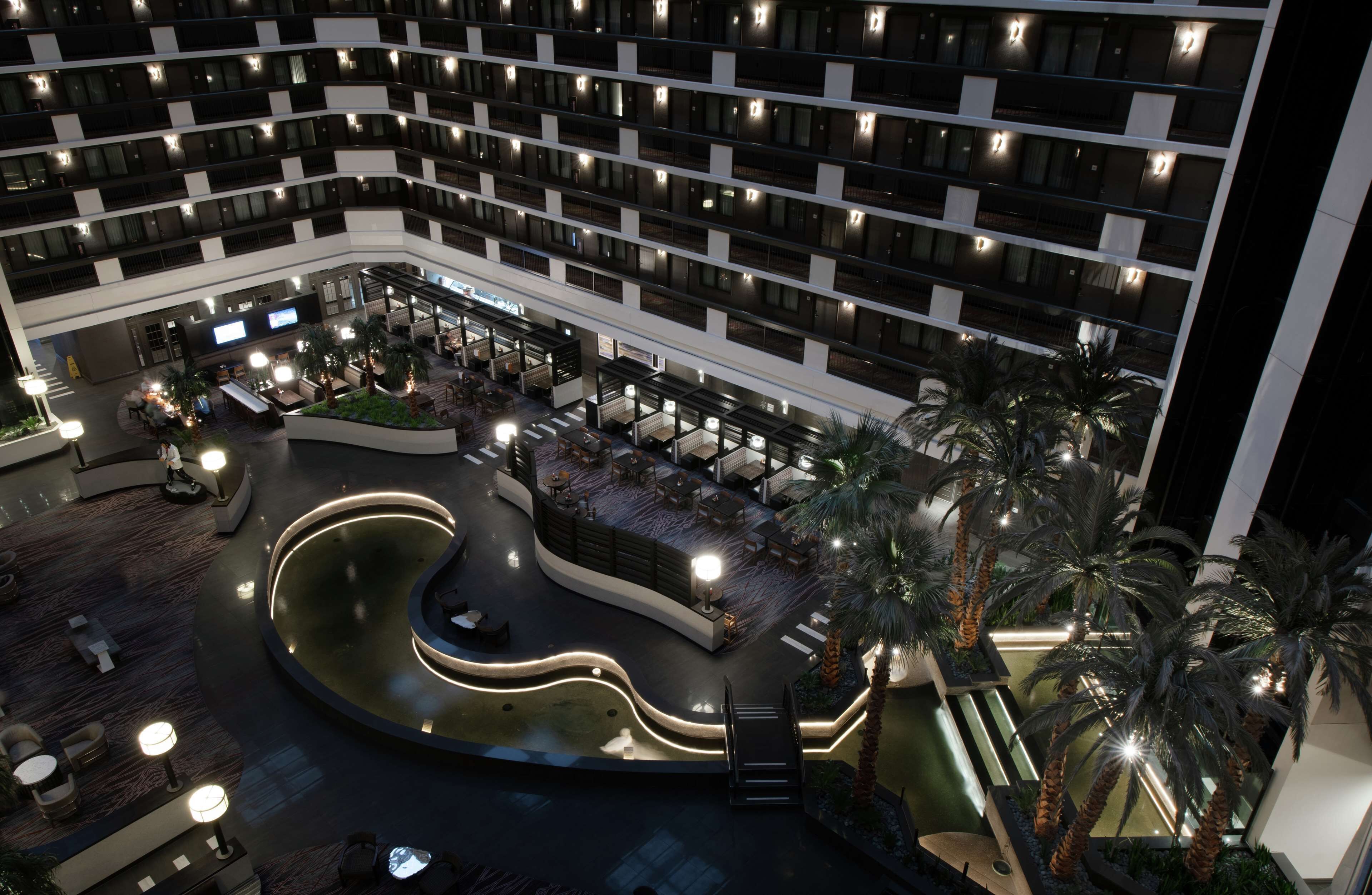 A multi-story hotel with a central courtyard featuring a water feature, outdoor seating, and palm trees.