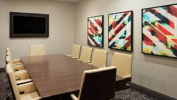 Un salón de conferencias con una mesa de madera oscura, sillas color beige y tres pinturas abstractas en la pared.