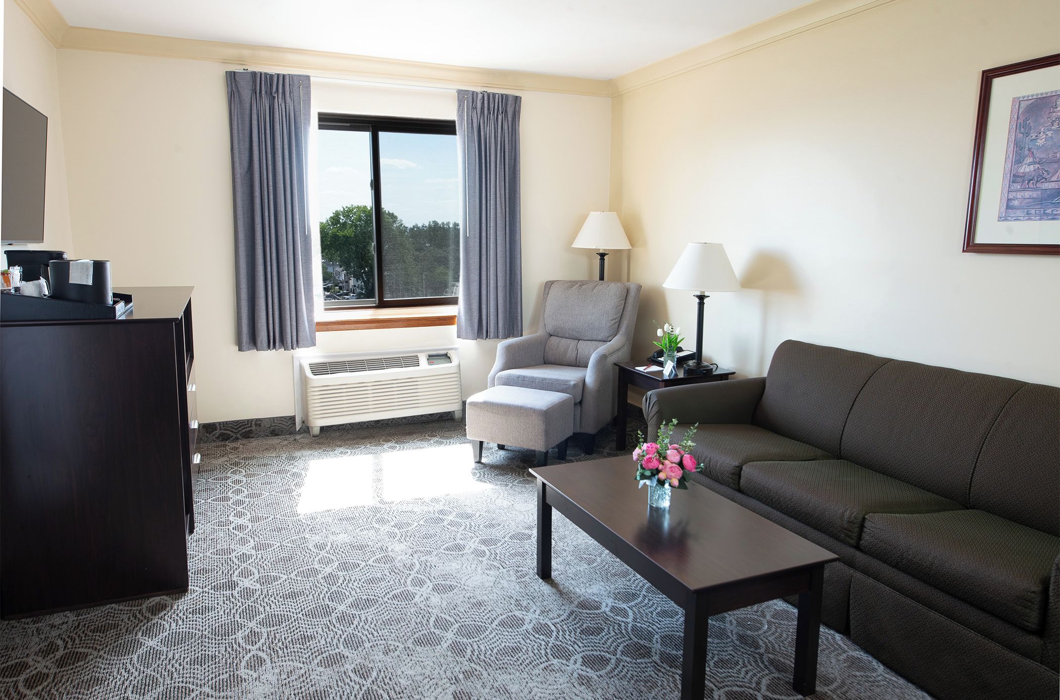 A hotel room with a desk, two chairs, a sofa, a coffee table, and a window with curtains.