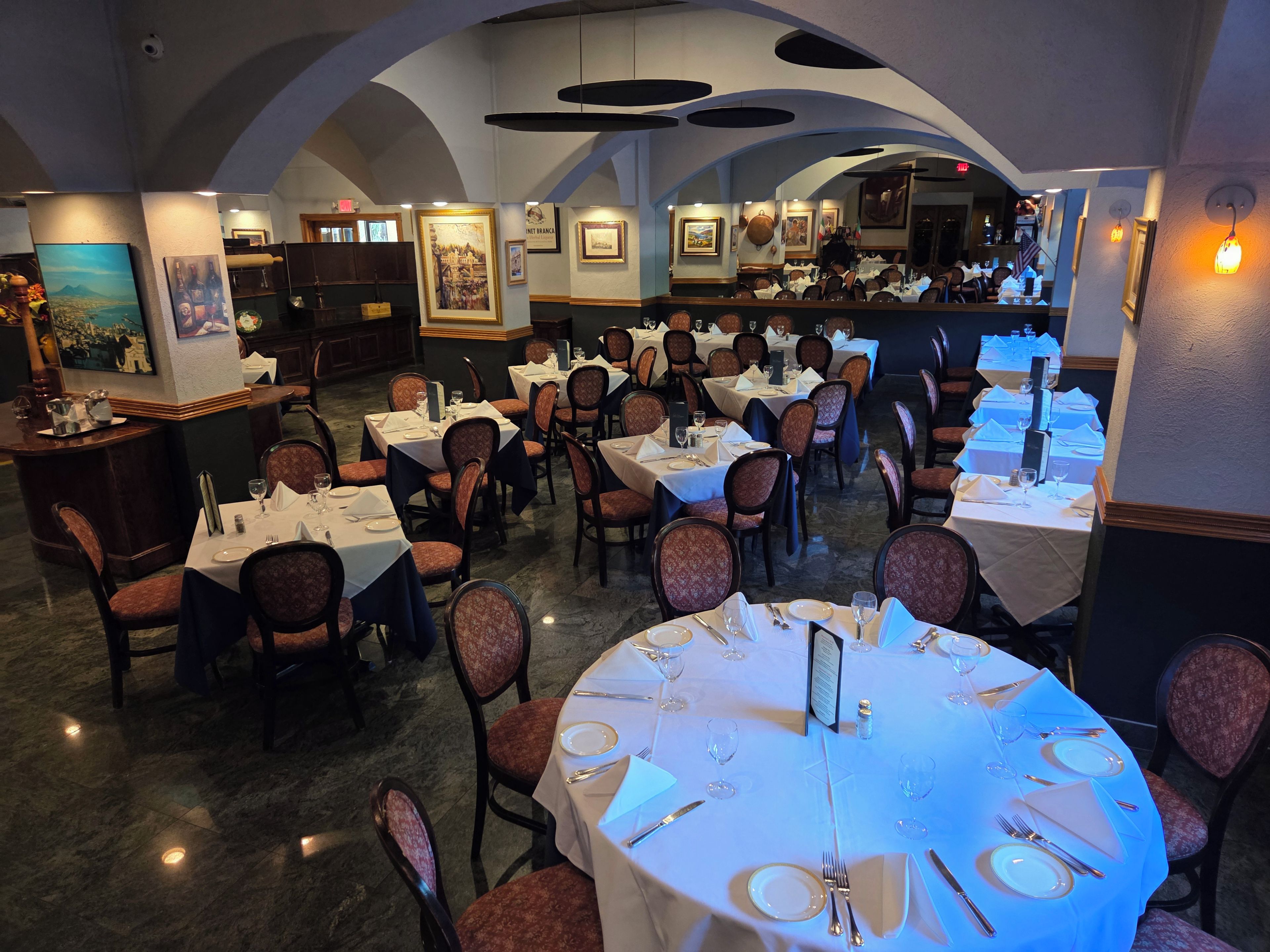 Ein Restaurant mit mehreren Tischen und Stühlen, einer Bar und gerahmten Kunstwerken an den Wänden.