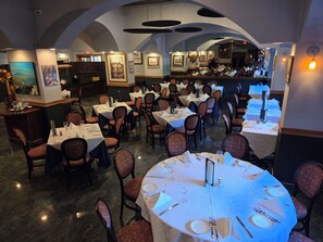 Un restaurante con varias mesas y sillas, una zona de bar y obras de arte enmarcadas en las paredes.
