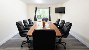 Un salón de conferencias con una larga mesa, sillas negras, un televisor de pantalla plana y un ventanal con cortinas.