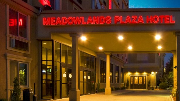 Exterior del Hotel Meadowlands Plaza, con una entrada destacada y señalización iluminada.