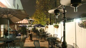 Un patio al aire libre con mesas, sillas, sombrillas y plantas colgantes.