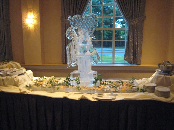 Una mesa de buffet con diversos platos, una escultura de vidrio decorativa y una ventana con cortinas.