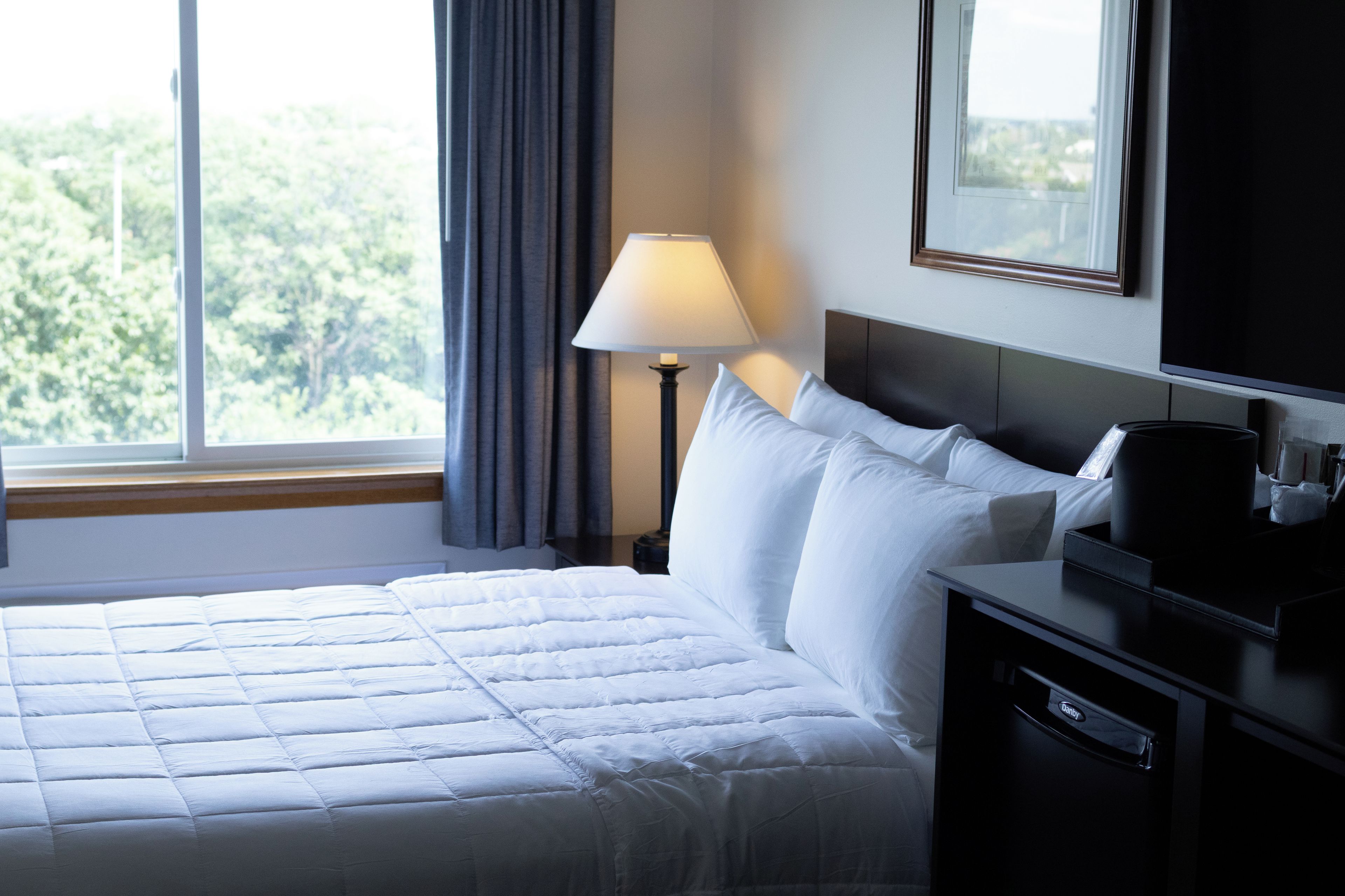 Habitación de hotel con cama, mesita de noche, lámpara, televisión y ventana con cortinas.