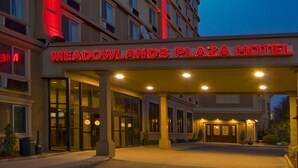 Un hotel con un cartel rojo llamativo que dice "MEADOWLANDS PLAZA HOTEL" y una entrada amplia con puertas de vidrio.