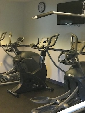 Three stationary bikes in a room with a clock on the wall. - Meadowlands Plaza Hotel (Secaucus)