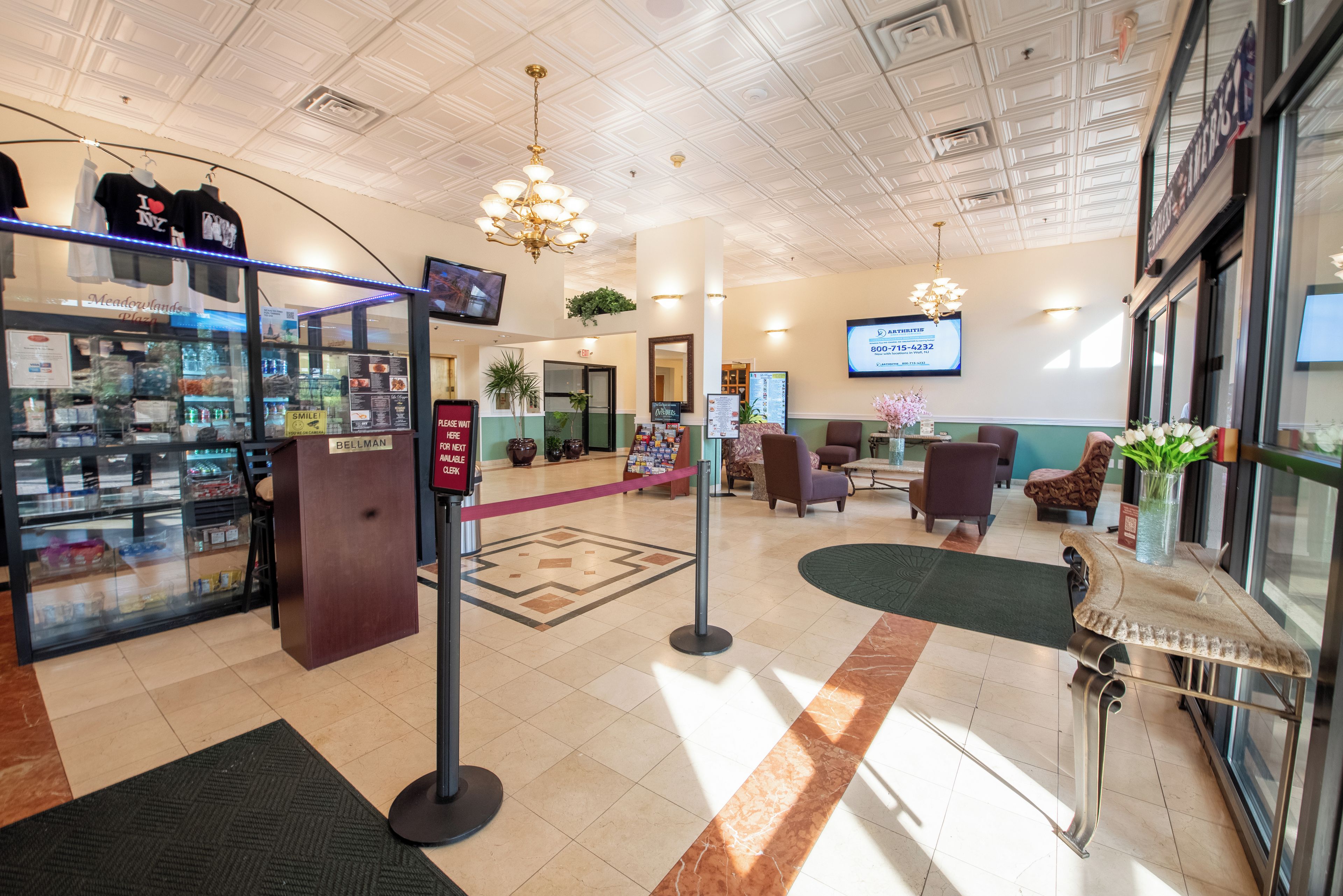 A hotel lobby with a reception desk, a waiting area with chairs, a glass display case, and a chandelier.