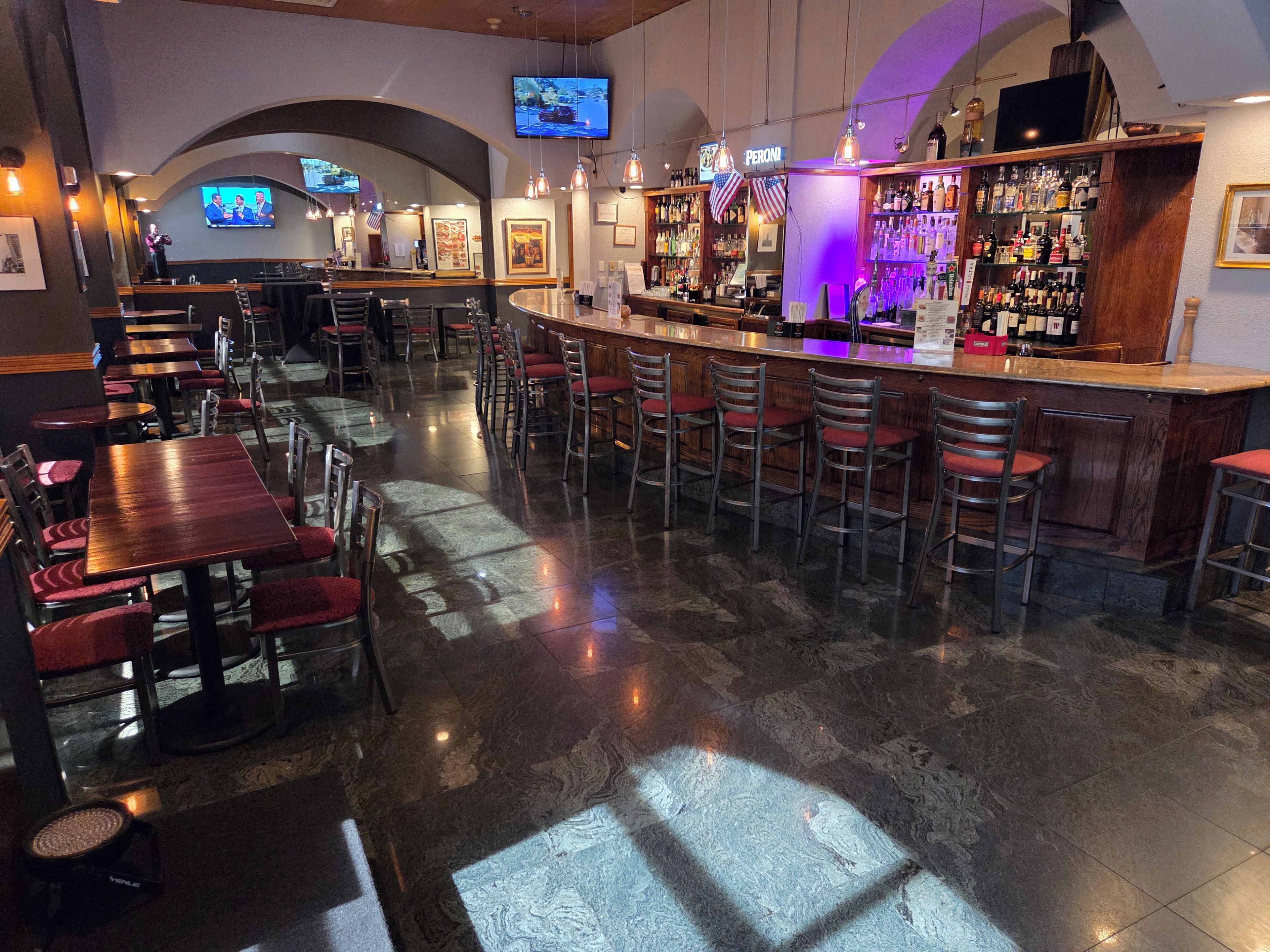 A bar area with multiple seating options, a television screen, and a variety of bottles on shelves.