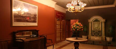 A lobby with a chandelier, a framed historical photograph, a reception desk, and a decorative fountain.