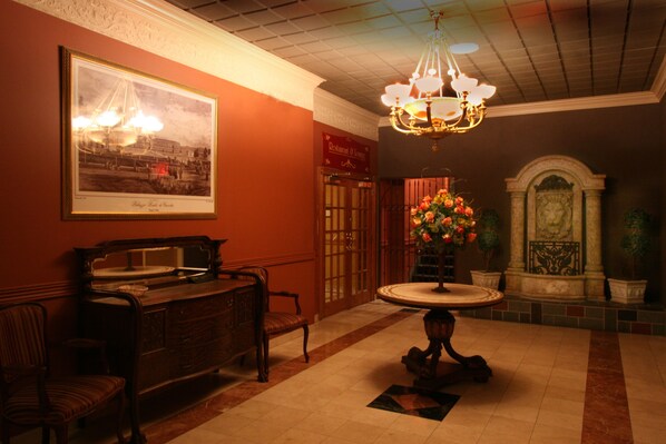 A lobby with a chandelier, a framed historical photograph, a reception desk, and a decorative fountain. - Meadowlands Plaza Hotel (Secaucus)
