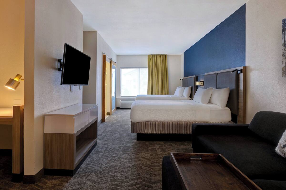 A hotel room with a bed, a TV mounted on the wall, a desk, and a sofa.