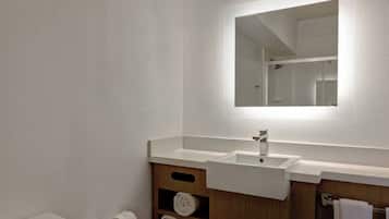 Une salle de bain moderne avec un lavabo blanc, un miroir et une étagère en bois où sont posées des serviettes.