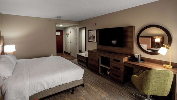 A hotel room with a bed, a desk with a flat-screen TV, a chair, and a mirror. - Hampton Inn Springfield (Springfield)
