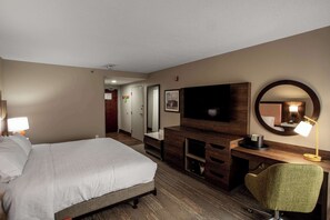 A hotel room with a bed, a desk with a flat-screen TV, a chair, and a mirror. - Hampton Inn Springfield (Springfield)