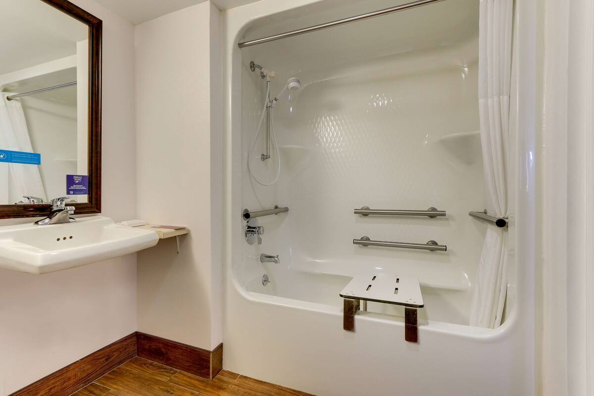 A bathroom with a white sink, a bathtub with a showerhead, and a mirror.