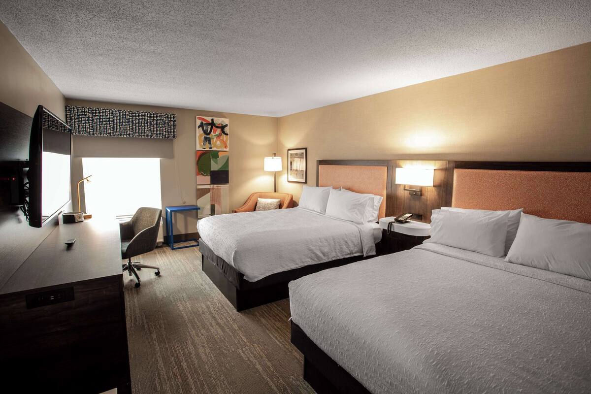 A hotel room with two beds, a desk, a chair, and a TV.